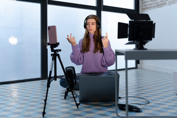 Portrait of young woman recording with laptop and smartphone in a studio