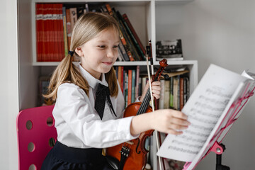 Smiling girl with violin looking at notes on the music stand