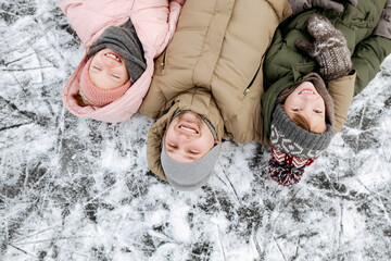 Family portrait of father and two children lying on ice in winter - obrazy, fototapety, plakaty