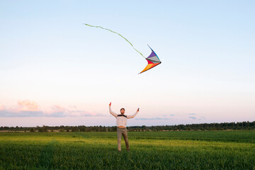 Mid adult man flying kite while standing on grassy landscape against sky at sunset