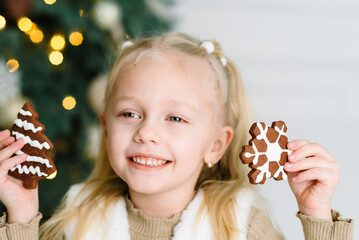 Merry Christmas and Happy Holidays. Child girl eating iced sugar cookies under Christmas tree Waiting for Christmas. Celebration New Year.