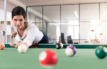 Determined businesswoman playing pool billard in modern office