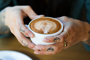 Tattooed hands holding cup of cappuchino