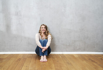 Smiling blond woman sitting on the floor in front of grey wall