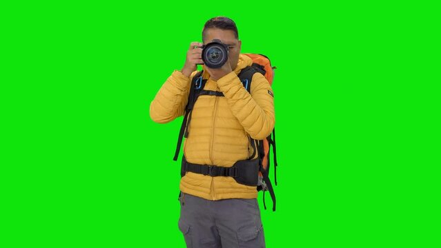 hiker with mountaineering backpack smiling and holding a camera in his hands then looking around while standing on a green screen background concept of screen, hiking, trip, 