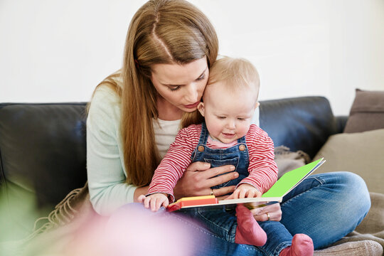 Mother and baby girl at home looking at book