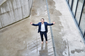 Smiling businessman standing barefoot in a puddle looking up
