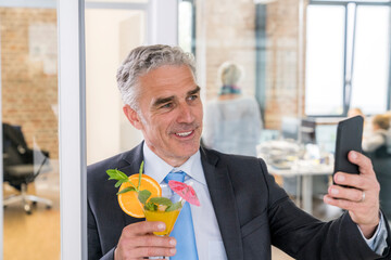 Mature businessman drinking cocktail while taking a selfie