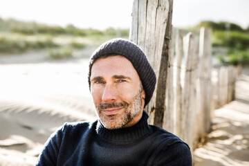 Portrait of smiling man at fence on the beach - obrazy, fototapety, plakaty
