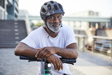 Portrait of smiling mature man wearing cycling helmet leaning on handlebar of Electric Scooter