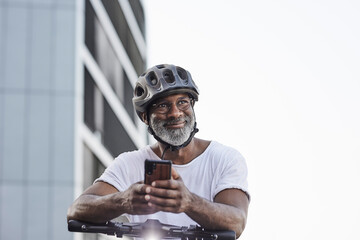 Portrait of happy mature man wearing cycling helmet leaning on handlebar of Electric Scooter