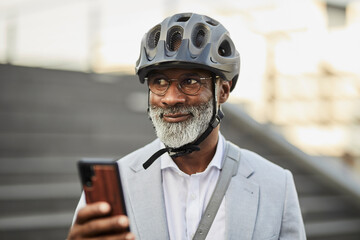 Portrait of smiling mature businessman with smartphone wearing cycling helmet and glasses