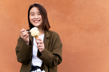 Happy young woman eating an ice cream cone at an orange wall