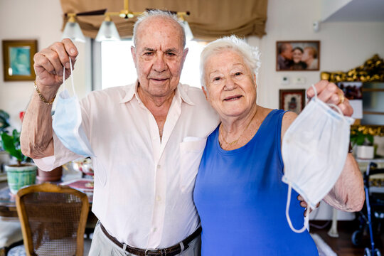 Senior couple holding protective masks at home - Powered by Adobe