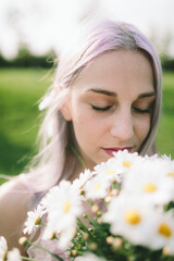 Woman with eyes closed holding bunch of daisies