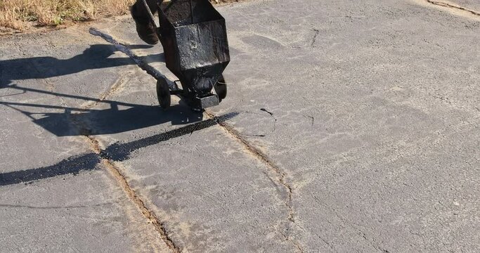 An asphalt patcher performs coated filling asphalt cracks sealing bitumen emulsion road surface restoration