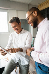 Two smiling businessmen with tablets having a meeting in loft office