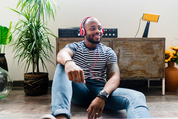 Smiling young man with headphones sitting on floor in a loft