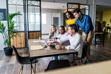 Business team having a meeting in loft office looking at laptop together