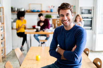 Portrait of smiling man at dining table at home with friends in background