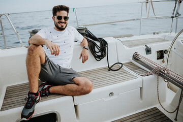 Smiling young man wearing sunglasses sitting in sailboat