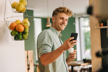 Young business owner drinking coffee, checking smartphone