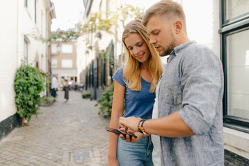 Netherlands, Maastricht, young couple looking at cell phone the city - obrazy, fototapety, plakaty