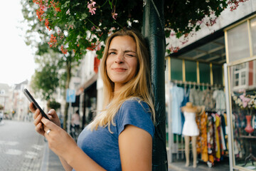Netherlands, Maastricht, smiling young woman with cell phone in the city twinkling