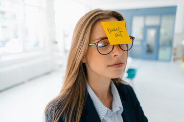 Young businesswman with yellow sticky note on her forehead