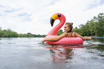 Young woman floating on a lake in a pink flamingo floating tire - obrazy, fototapety, plakaty