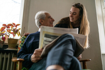 Happy young woman and senior man with newspaper at home