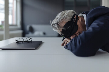 Senior businessman wearing eye mask lying on desk