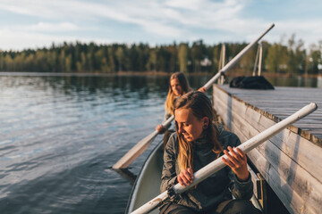Two young women boating on lake - obrazy, fototapety, plakaty