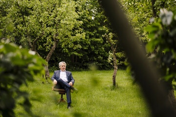 Senior businessman sitting on a chair in a rural garden