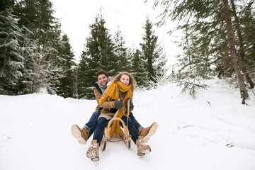 Happy young couple on sledge in winter forest