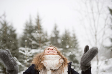 Happy young woman enjoying snowfall in winter forest