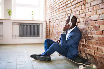 Businessman sitting on longboard listening to music with headphones