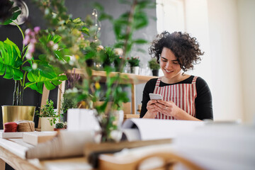 Smiling young woman using cell phone in a small shop with plants