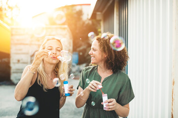 Two happy women blowing soap bubbles outdoors