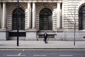 UK, London, stylish senior businessman with briefcase and umbrella standing on pavement