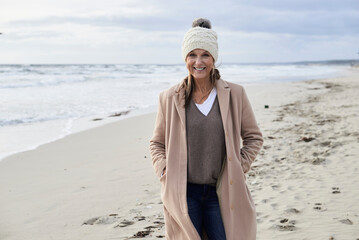 Spain, Menorca, portrait of smiling senior woman wearing bobble hat and coat on the beach in winter