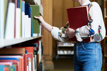 Female student with a book in a public library, choosing one