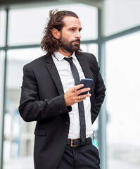 Portrait of bearded businessman standing indoors with smart phone in hand