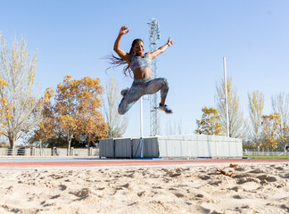 Cheerful sportswoman training for long jump over sand during sunny day