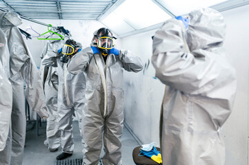 Team of sanitation workers wearing protective coveralls and gas masks while standing in locker room