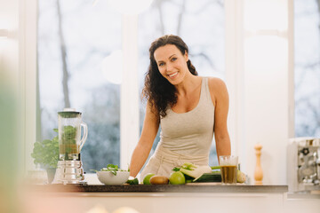 Fit woman standing in kitchen, preparing healthy smoothie