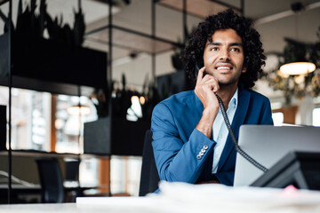Smiling businessman talking on telephone while sitting with laptop at office