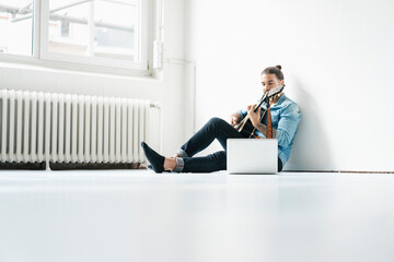 Man sitting with laptop on floor playing guitar