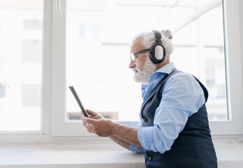 Mature man with tablet and headphones at the window