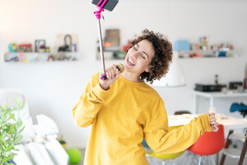 Carefree woman at home singing into microphone attached to a selfie stick